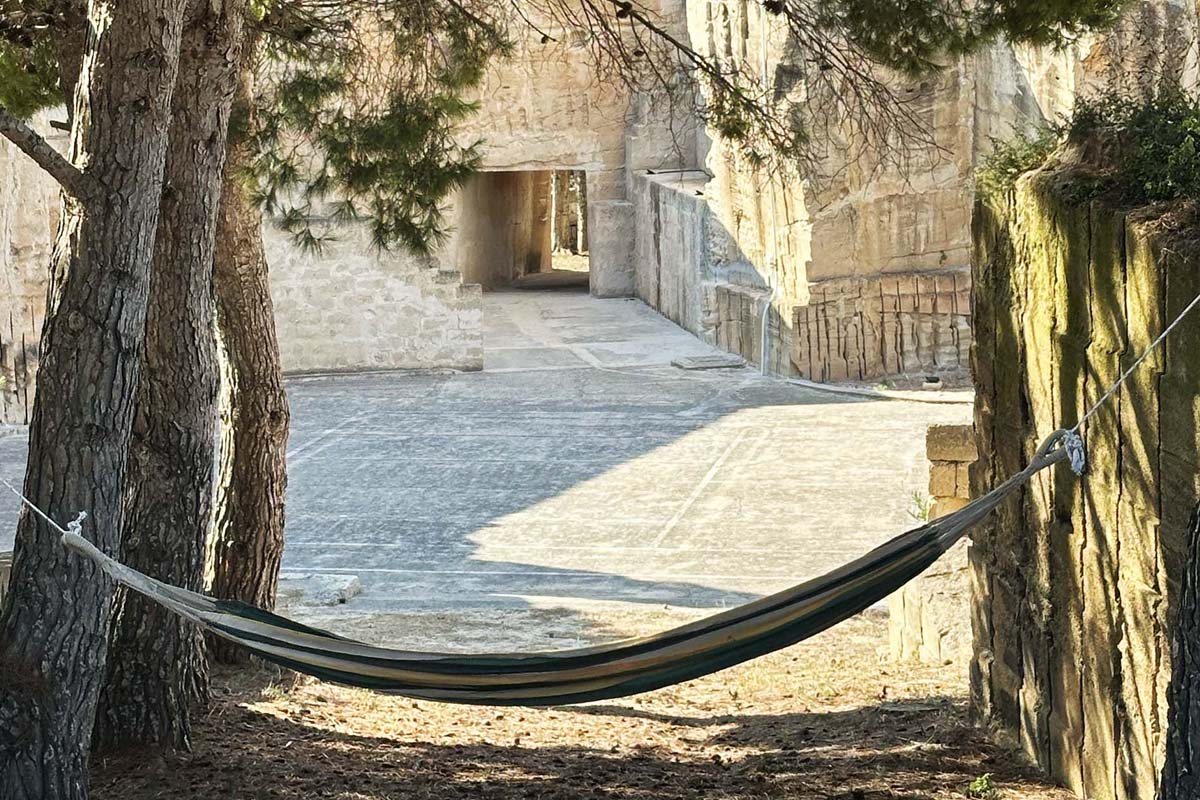 Angolo relax negli esterni di Mae a Favignana con amaca tra gli alberi e vista sulla cava di tufo.