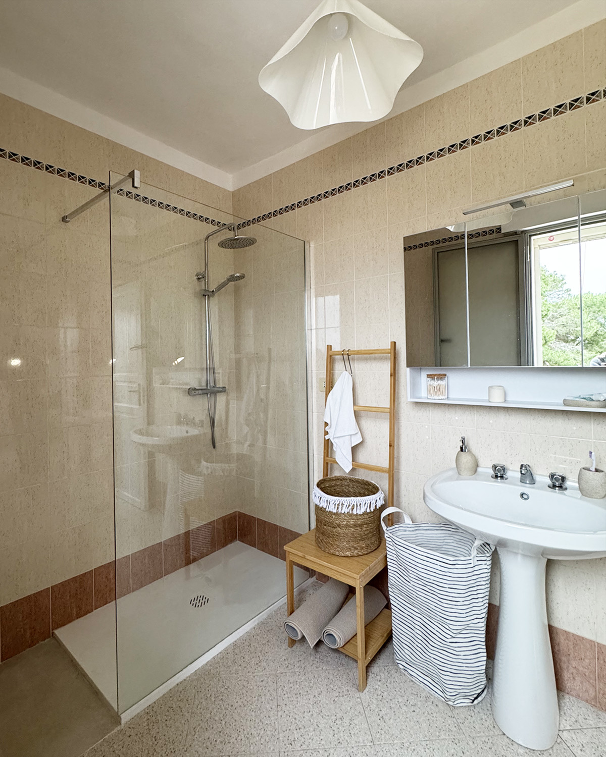 Bagno luminoso di Mae a Favignana con ampia doccia in vetro, lavabo bianco e dettagli in legno naturale.