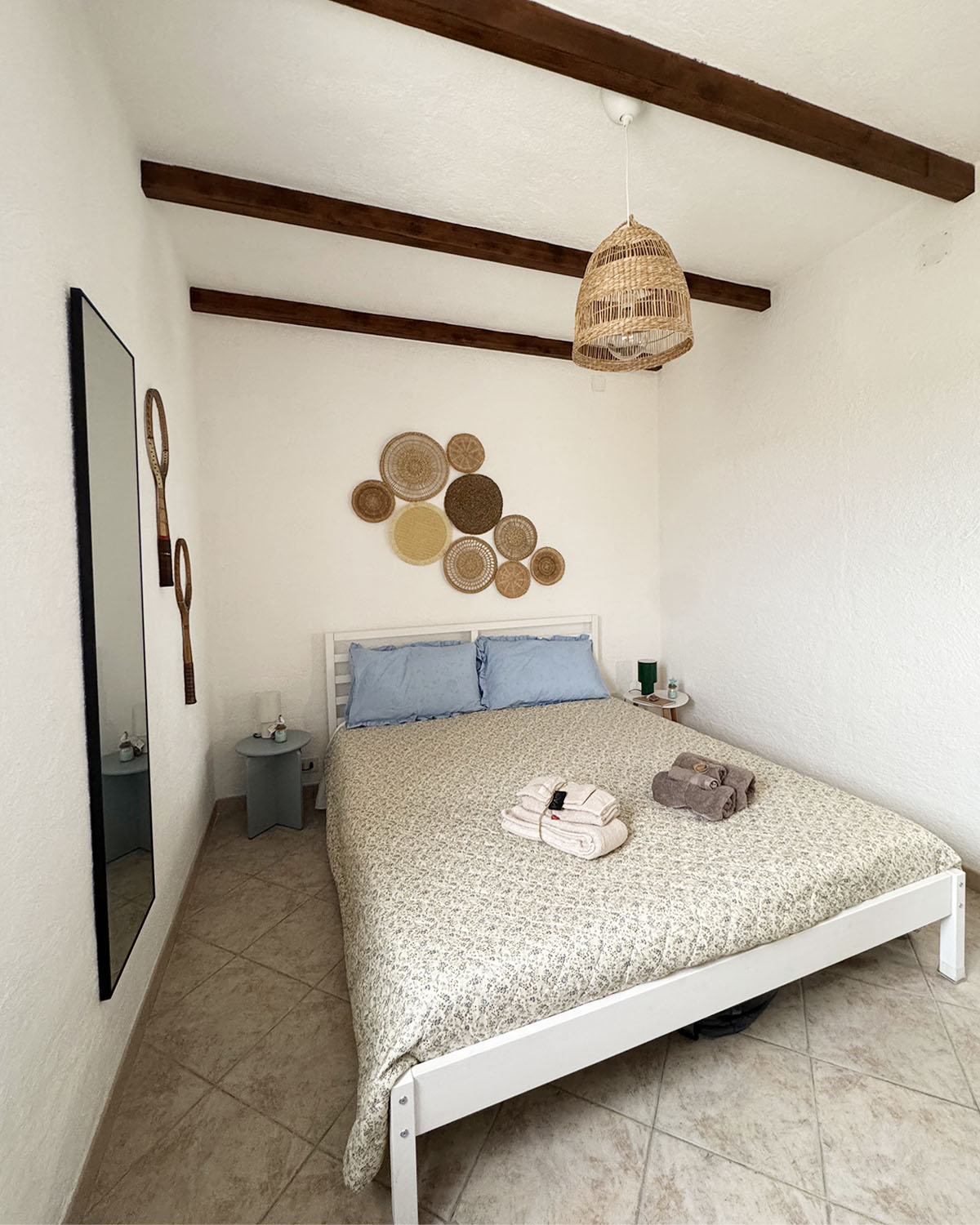 Camera doppia di Mae a Favignana con letto matrimoniale, cuscini azzurri, travi in legno a vista e arredi essenziali in stile naturale.
