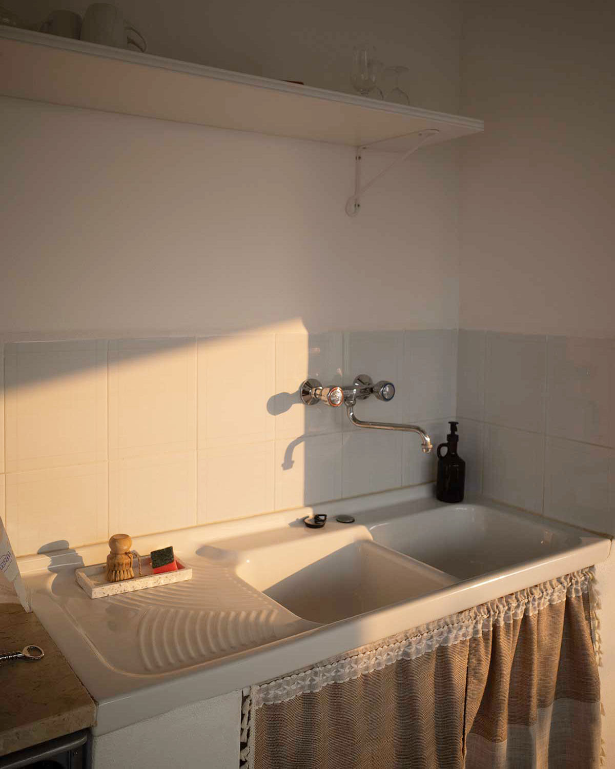 Dettaglio della cucina di Mae a Favignana con lavello bianco, luce calda del sole e tessili dai toni naturali.