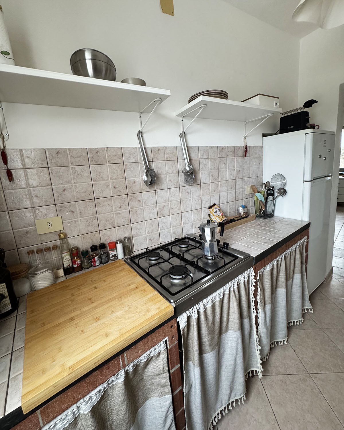 Cucina di Mae a Favignana con piano cottura, frigorifero, mensole a vista e dettagli essenziali dallo stile mediterraneo.