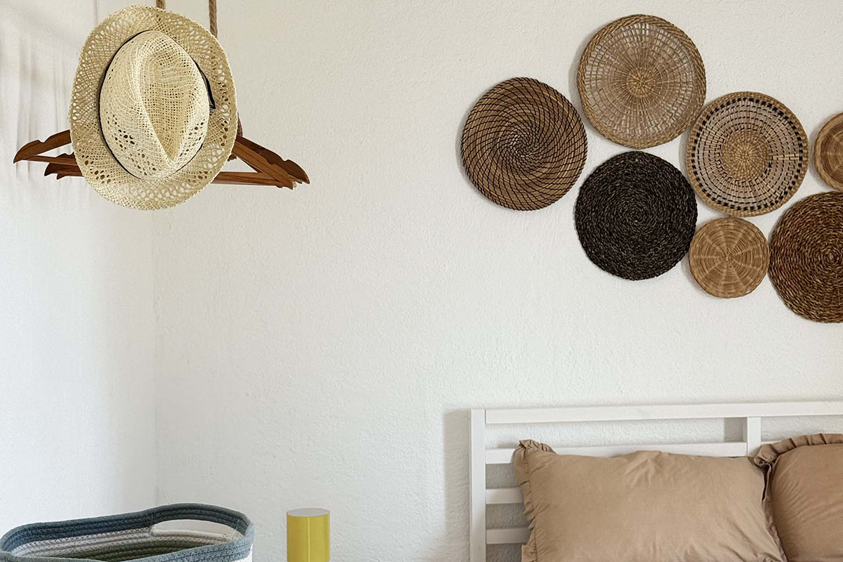 Dettaglio della camera di Mae a Favignana con cappello in paglia, letto matrimoniale e decorazioni intrecciate sulla parete.