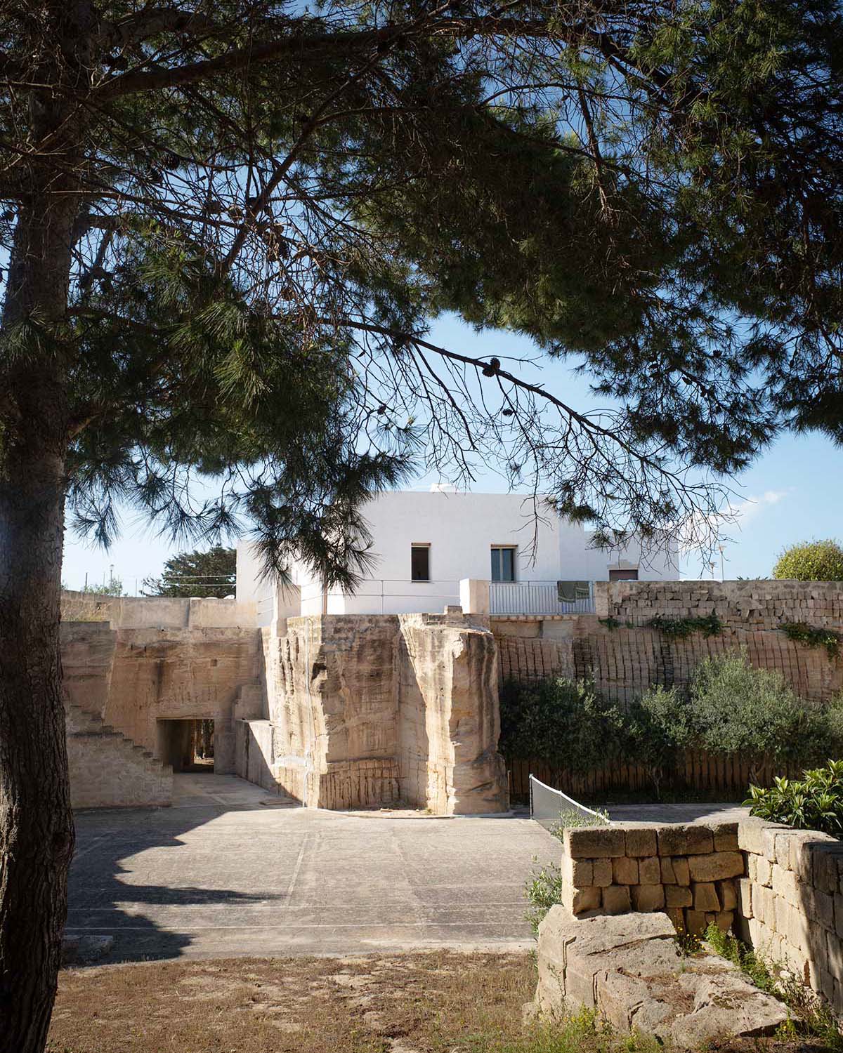 Spazio esterno di Mae a Favignana con campo da tennis, alberi ombreggianti e cava di tufo privata sullo sfondo.