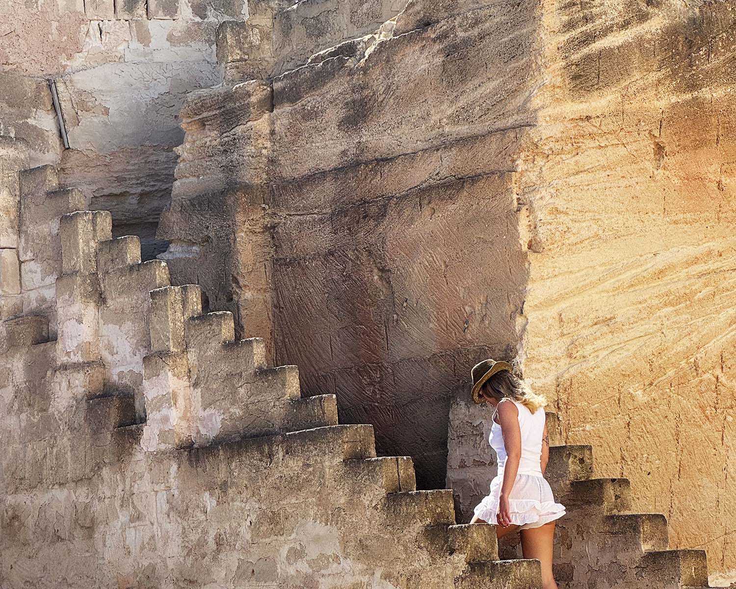 Scorcio della cava di tufo di Mae a Favignana con scale in pietra e una ragazza con cappello le attraversa