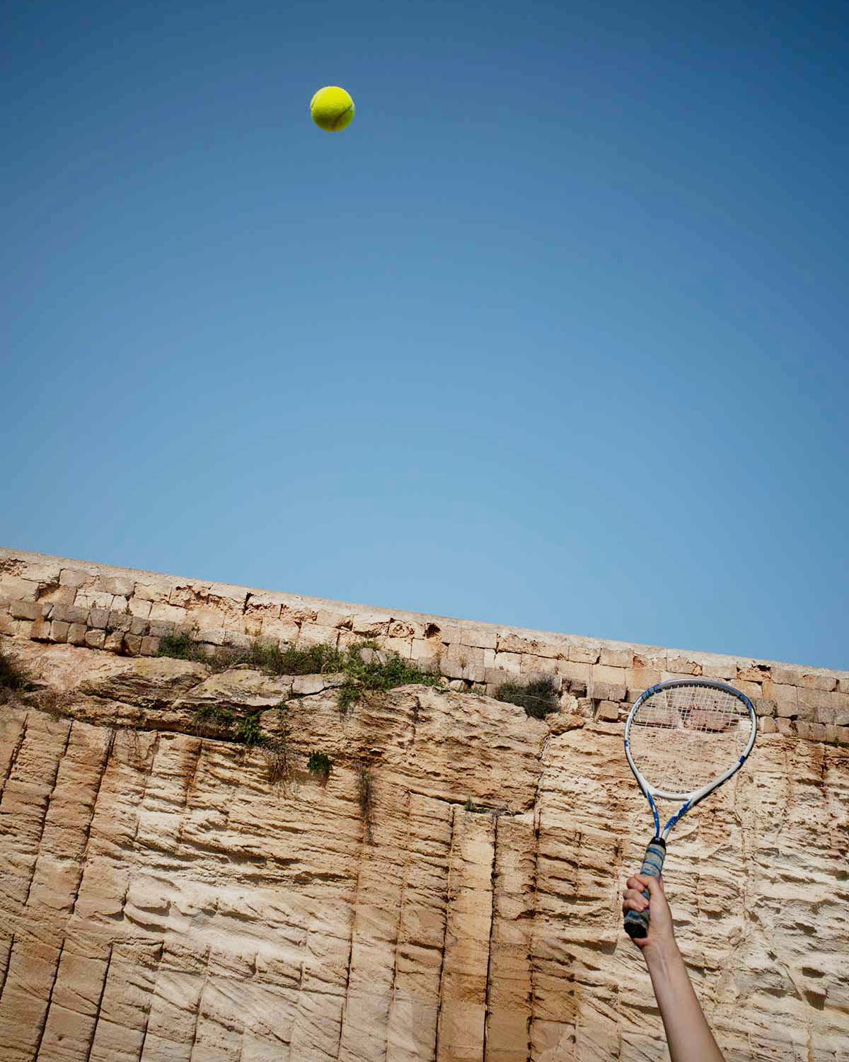 Momento di gioco nel campo da tennis di Mae a Favignana, tra cielo limpido, racchetta in movimento e pareti in tufo sullo sfondo.