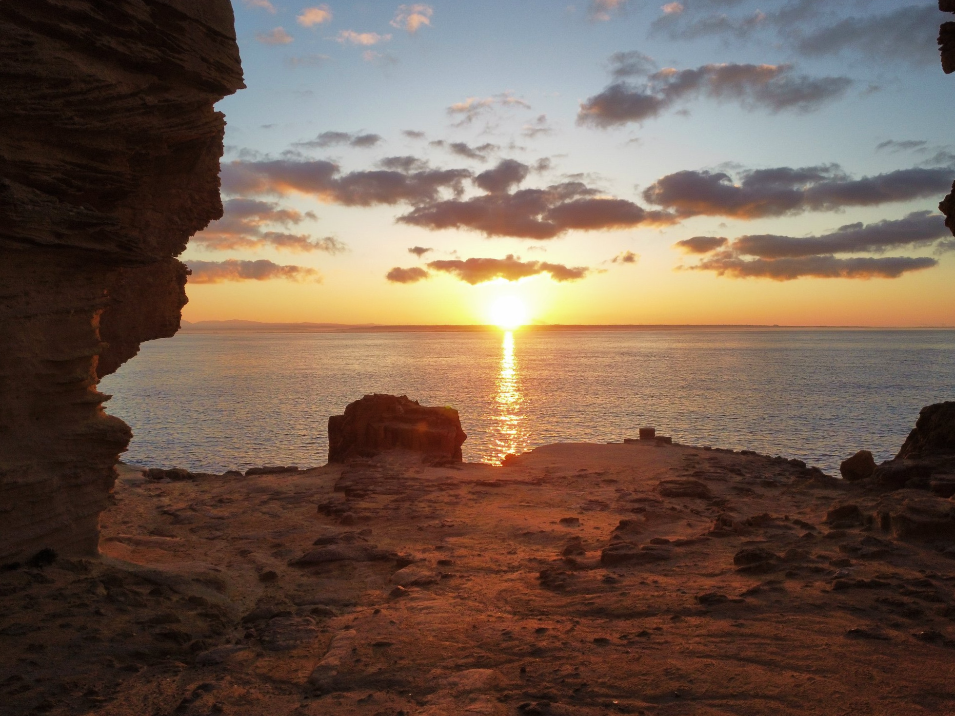 Scorcio della costa di Favignana vicino alla spiaggia del Bue Marino, con sole che tramonta all'orizzonte riflettendosi sul mare