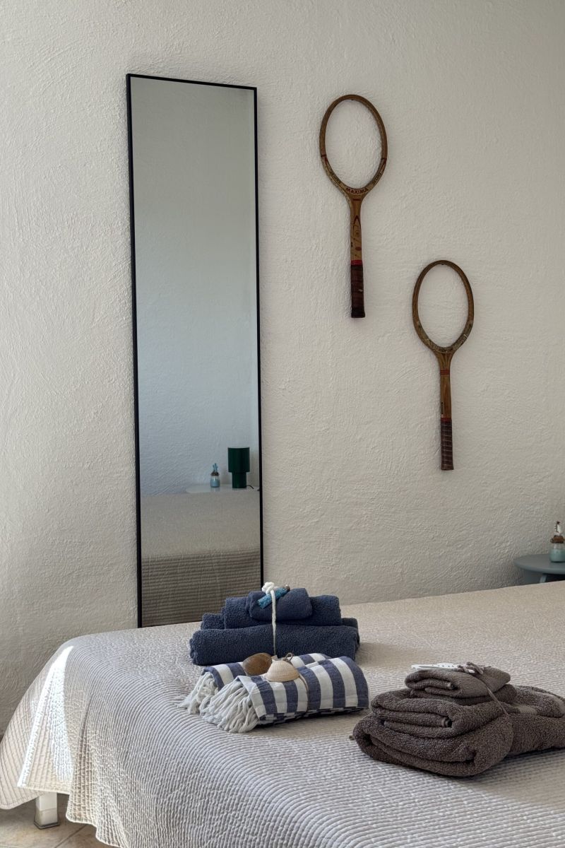 dettaglio stanza con letto matrimoniale su cui sono appoggiati asciugamani piegati per gli ospiti, parete alle spalle con specchio e racchette da tennis appese