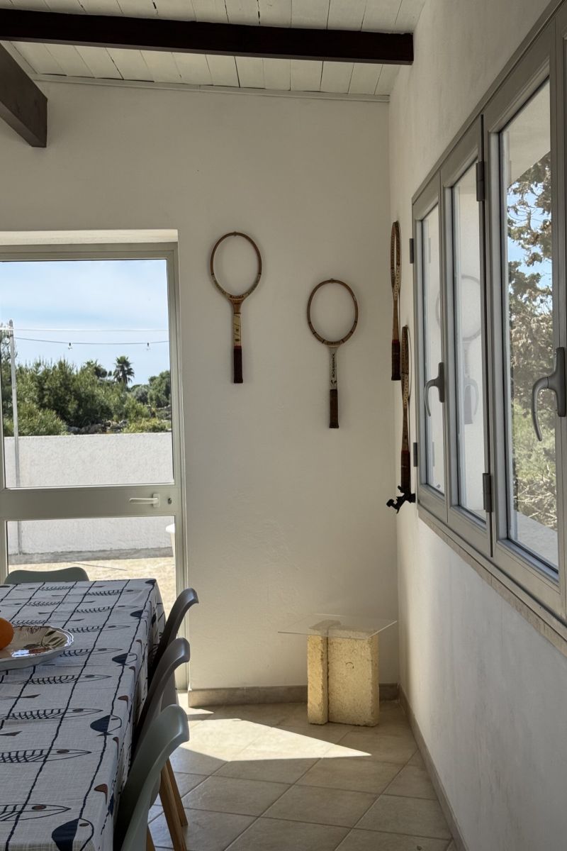 dettaglio delle sala da pranzo luminosa con grandi finestre, tavolo, racchette da tennis appese alle pareti e