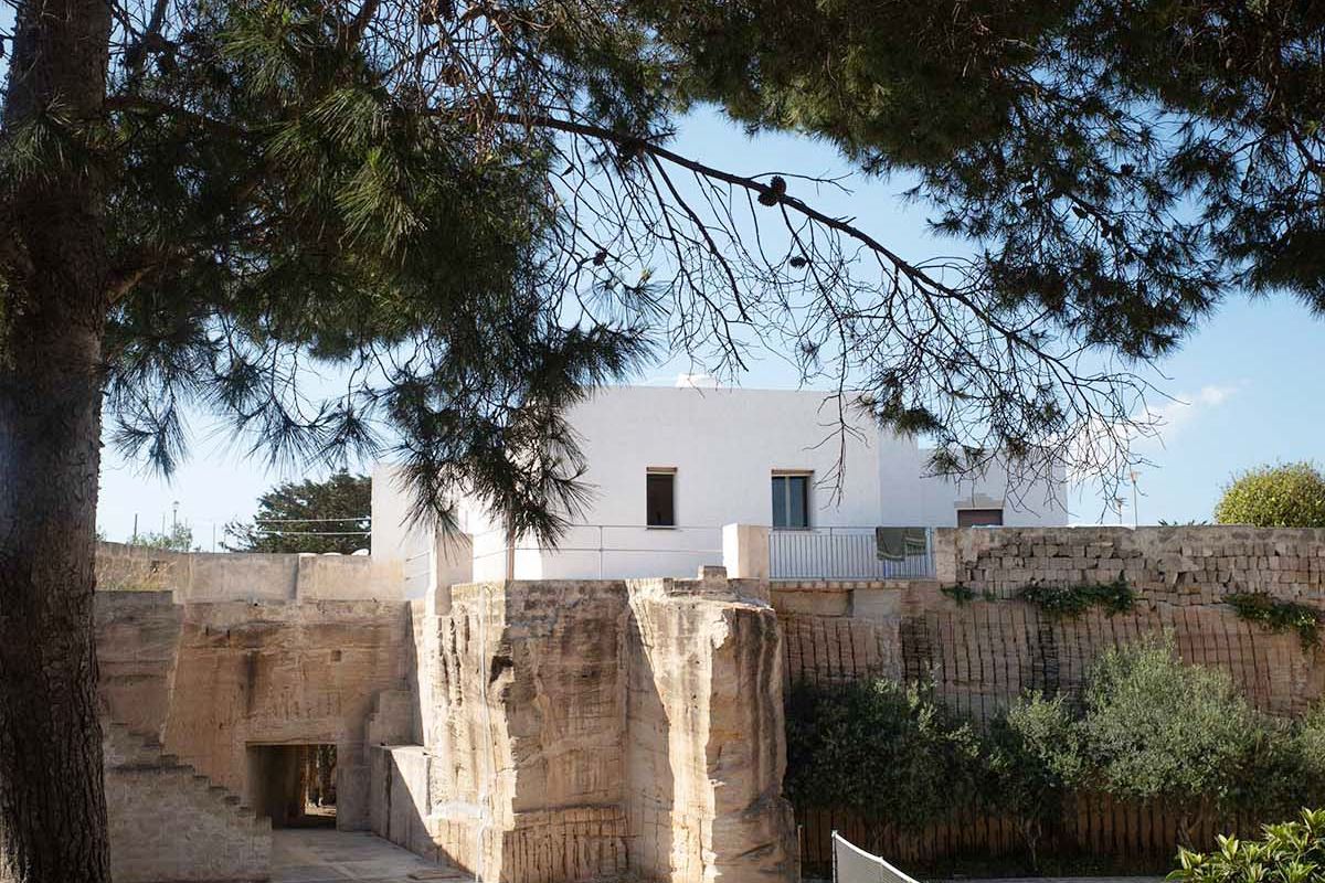 Spazio esterno di Mae a Favignana con campo da tennis, alberi ombreggianti e cava di tufo privata sullo sfondo.